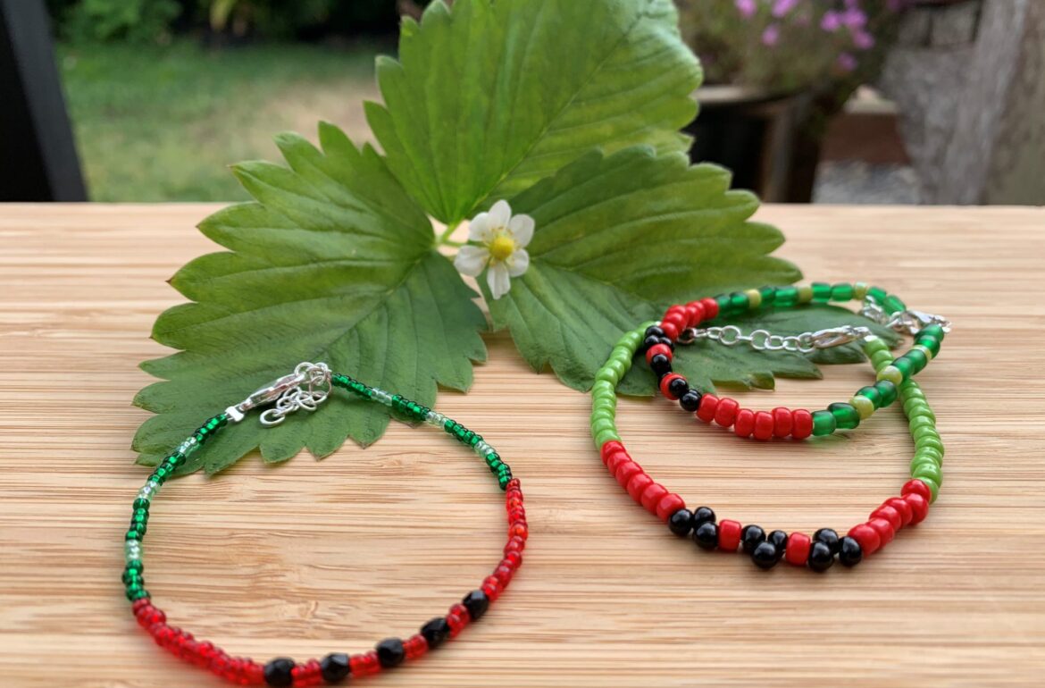 Two bracelets with red, green and black beads on a wooden table.