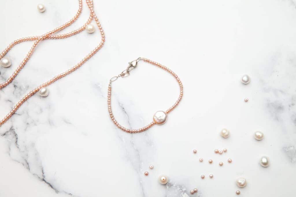 A rose gold bracelet with pearls on a marble table.