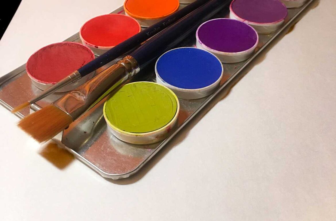 A tray of paints and brushes on a white surface.