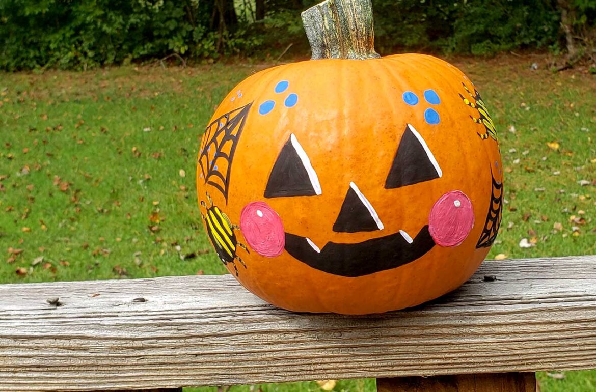 A painted pumpkin sitting on a wooden bench.