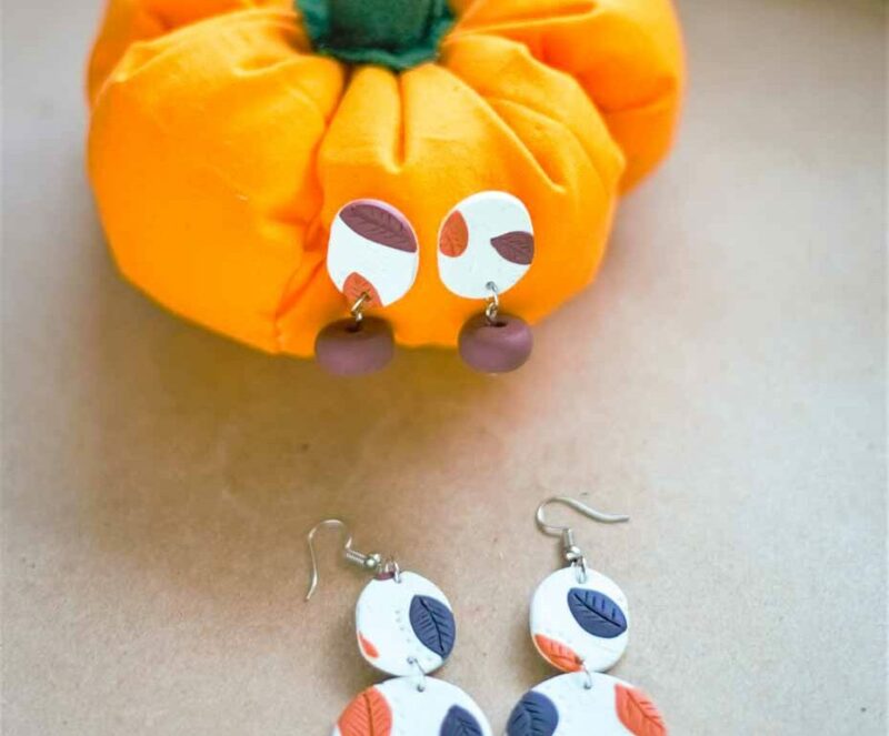 A pair of earrings and a pumpkin on a table.