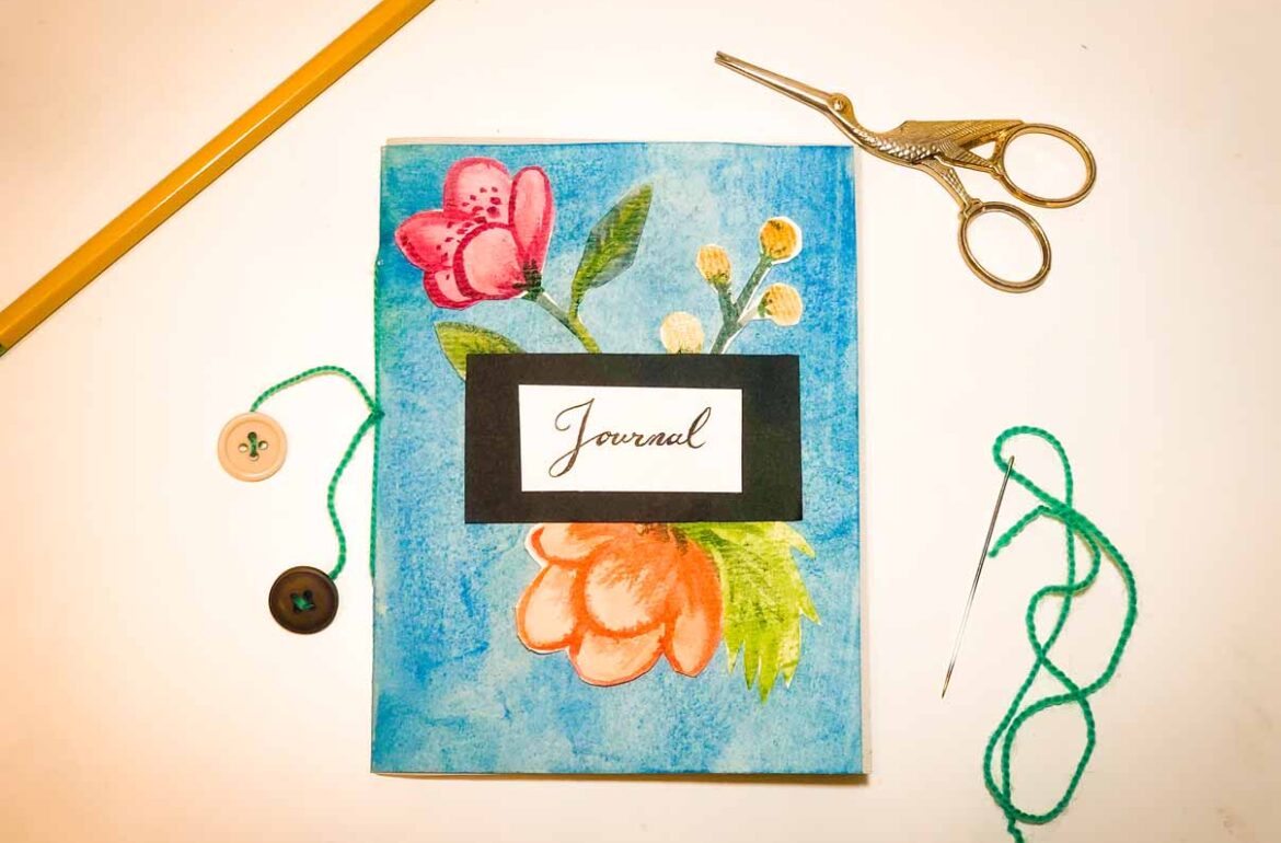A journal with flowers and scissors next to it.