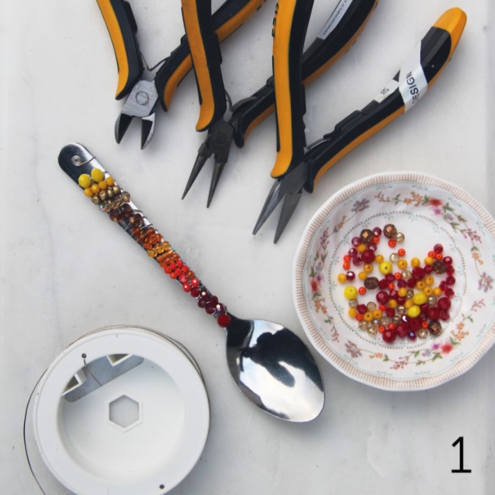A bowl of beads, pliers and a spoon.
