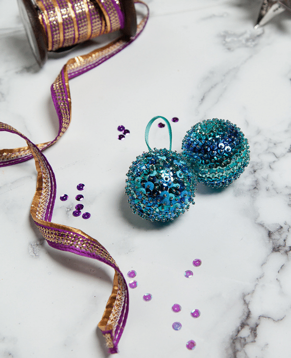 Two blue and purple christmas ornaments on a marble table.