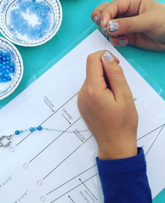 A child is making a bead necklace on a piece of paper.