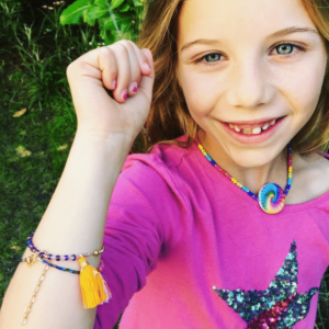 A little girl wearing a pink shirt and tassel bracelet.