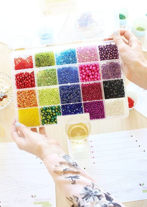A person holding a colorful beading kit on a table.