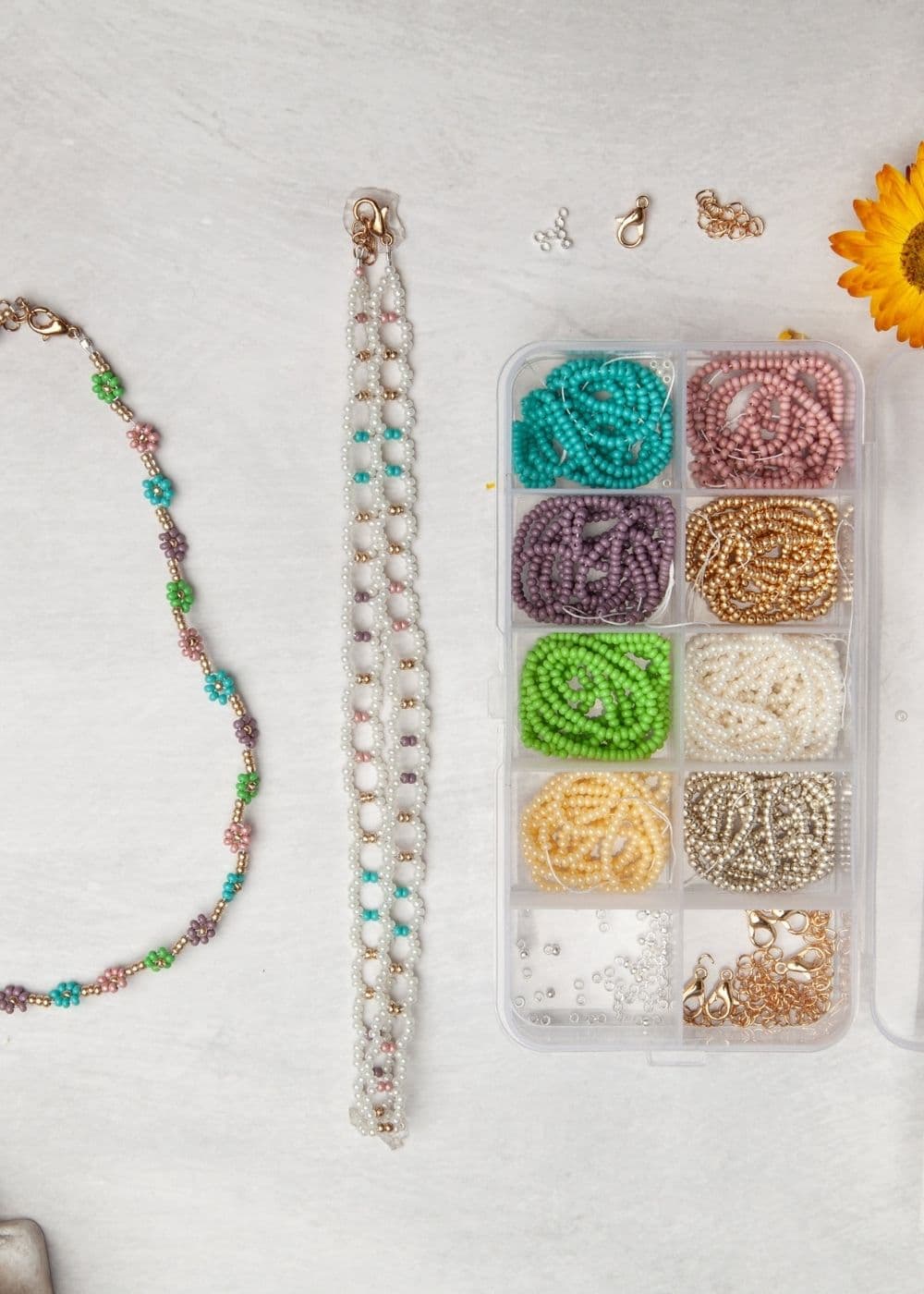 A box of beads, necklaces, and a flower on a table.