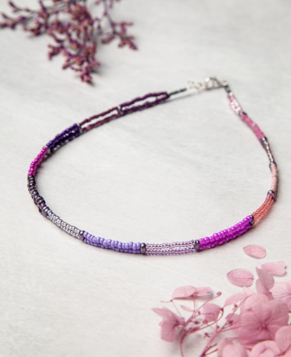 A purple and pink beaded necklace on a white surface.