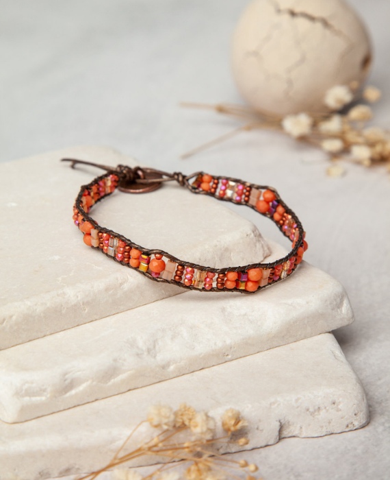 A bracelet with orange and brown beads on top of a stone.