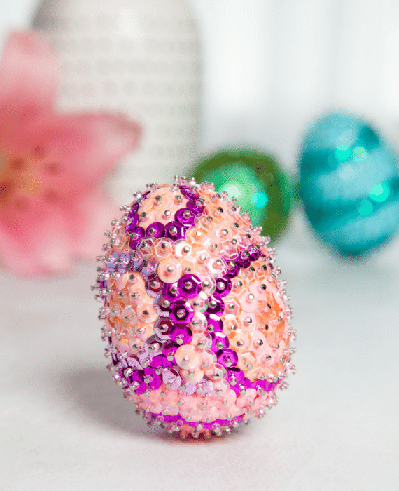 Sequin easter eggs on a table next to a flower.