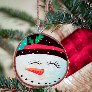A snowman ornament hangs on a christmas tree.