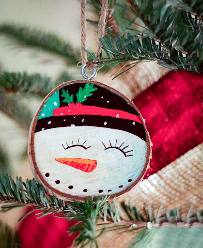 A snowman ornament hangs on a christmas tree.