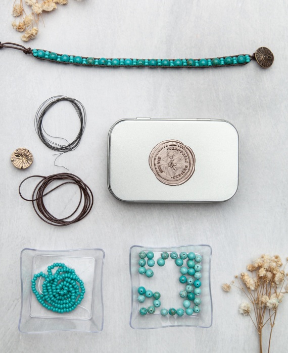 A tin with turquoise beads and other items on it.