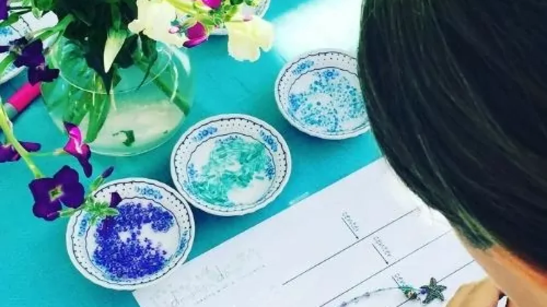 A girl is hosting a Kids Jewelry Making Party - Bay Area at a table with flowers.